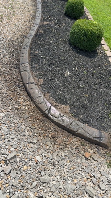 Curved stamped curbing separating gravel from a mulched garden bed
